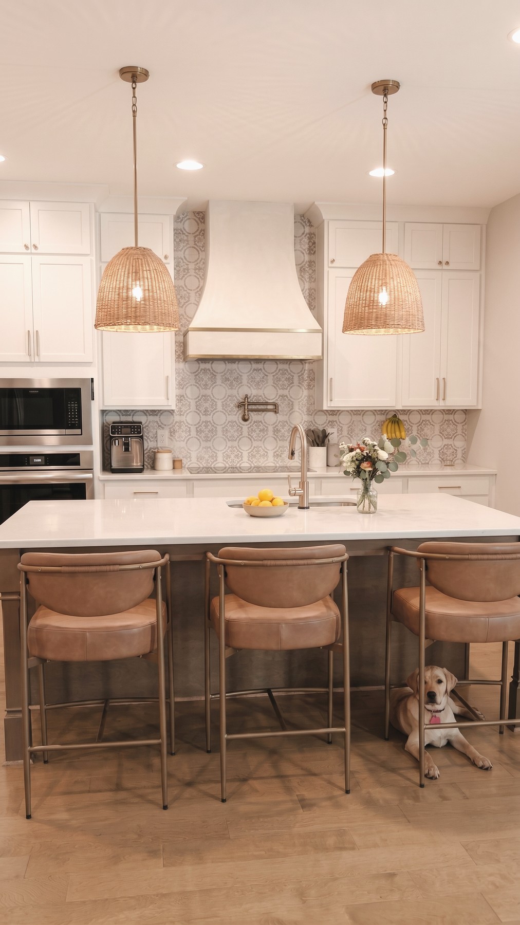 A bright white kitchen with rattan pendant lights and a bowl of lemons on the island